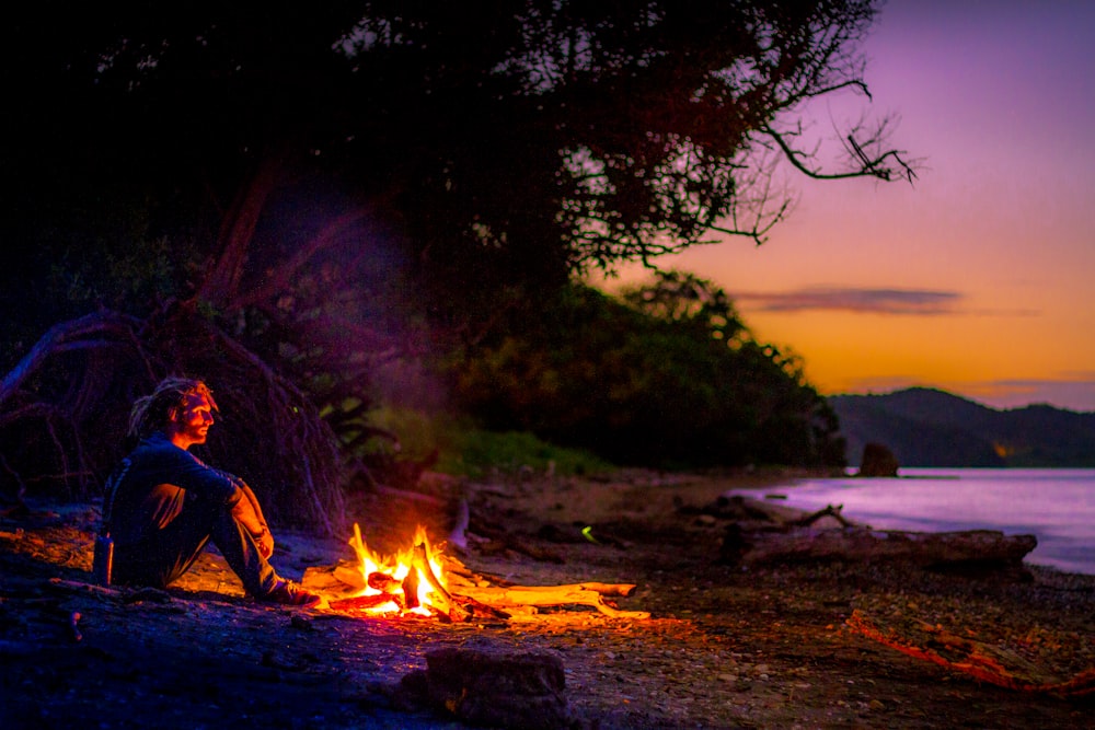 man sitting on ground near bonfire during night time