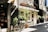 A cozy street with a brick building housing an Italian restaurant named 'Mama Leone'. There are two potted plants and a bicycle parked in front. To the left, part of a shop entrance with various items on display is visible. A person wearing a red shirt is walking further down the cobblestone path.