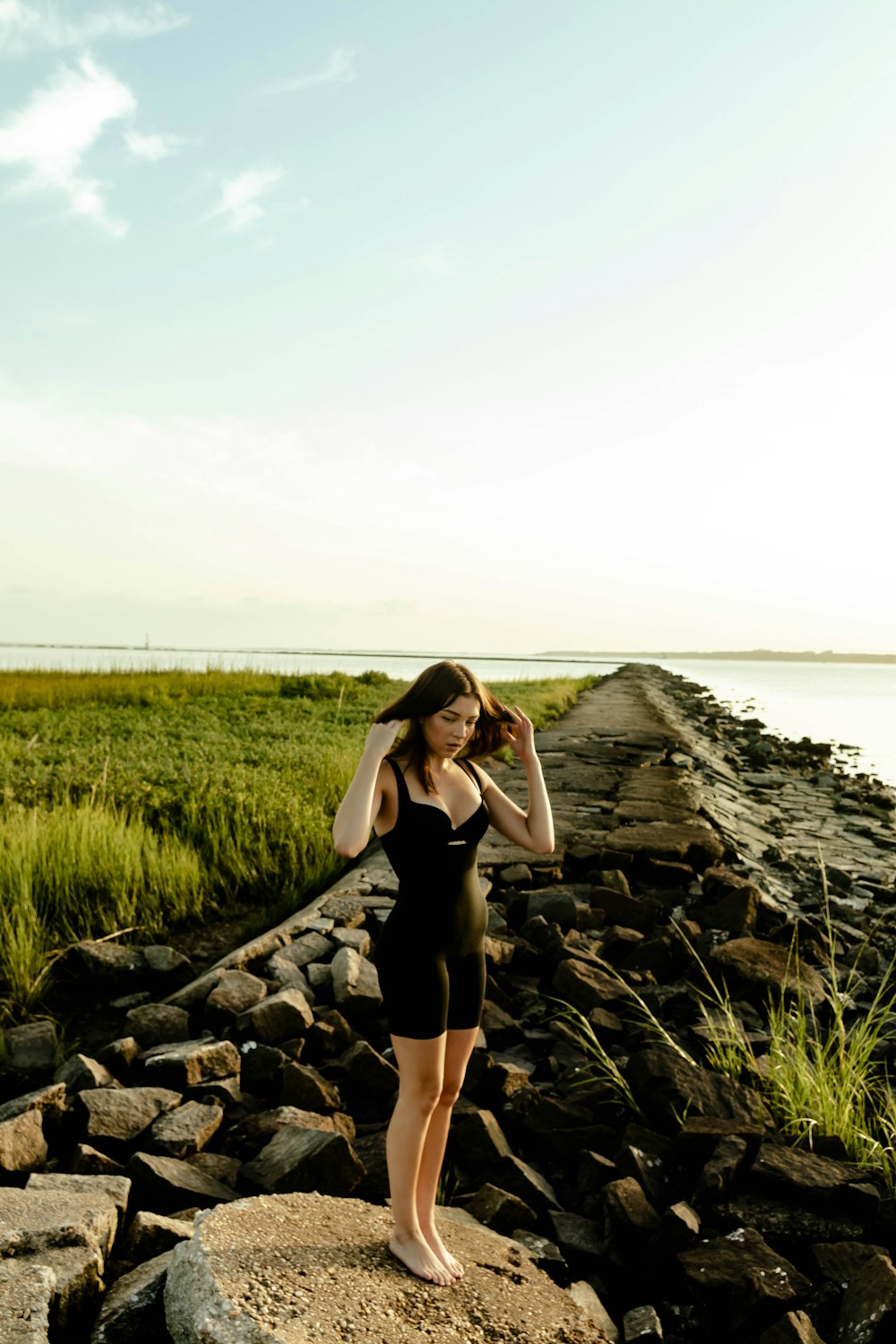 woman in black tank top and black skirt standing on rocky shore during daytime