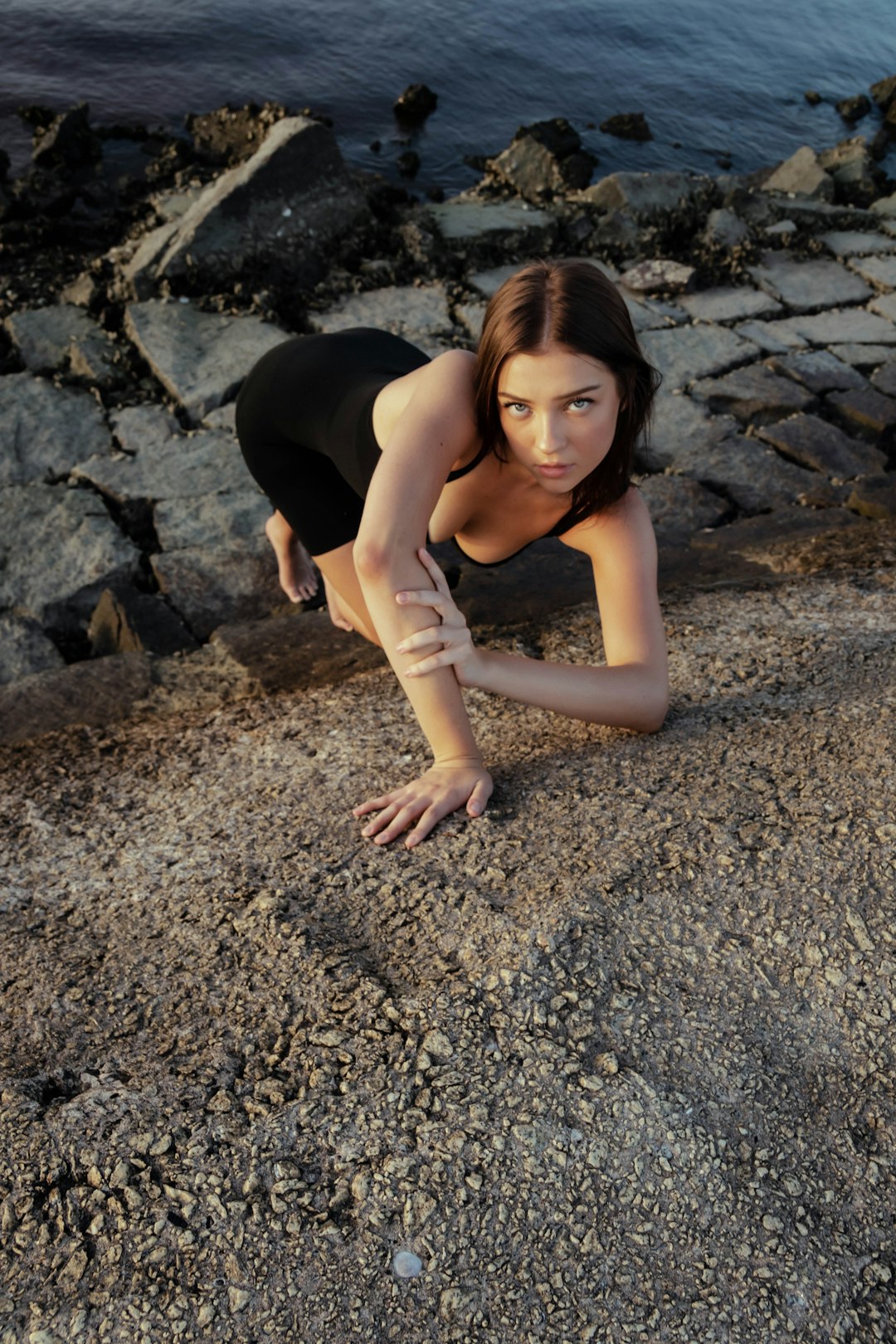 woman in black tank top and black pants lying on gray rocky ground during daytime
