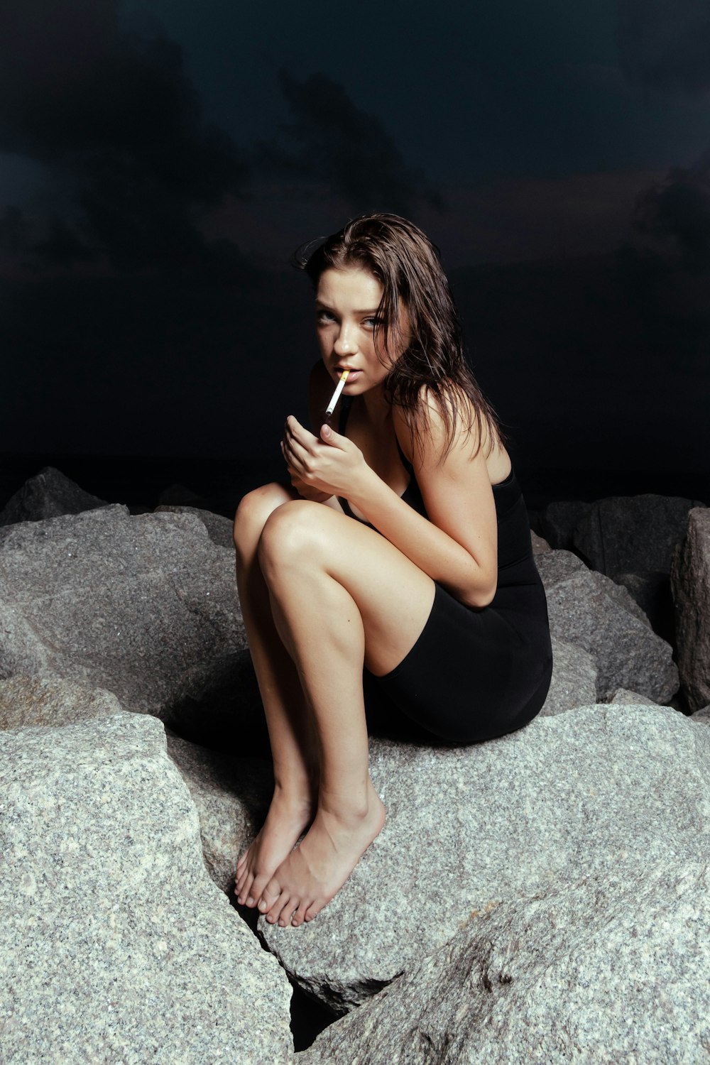 woman in black tank top and black shorts sitting on gray rock