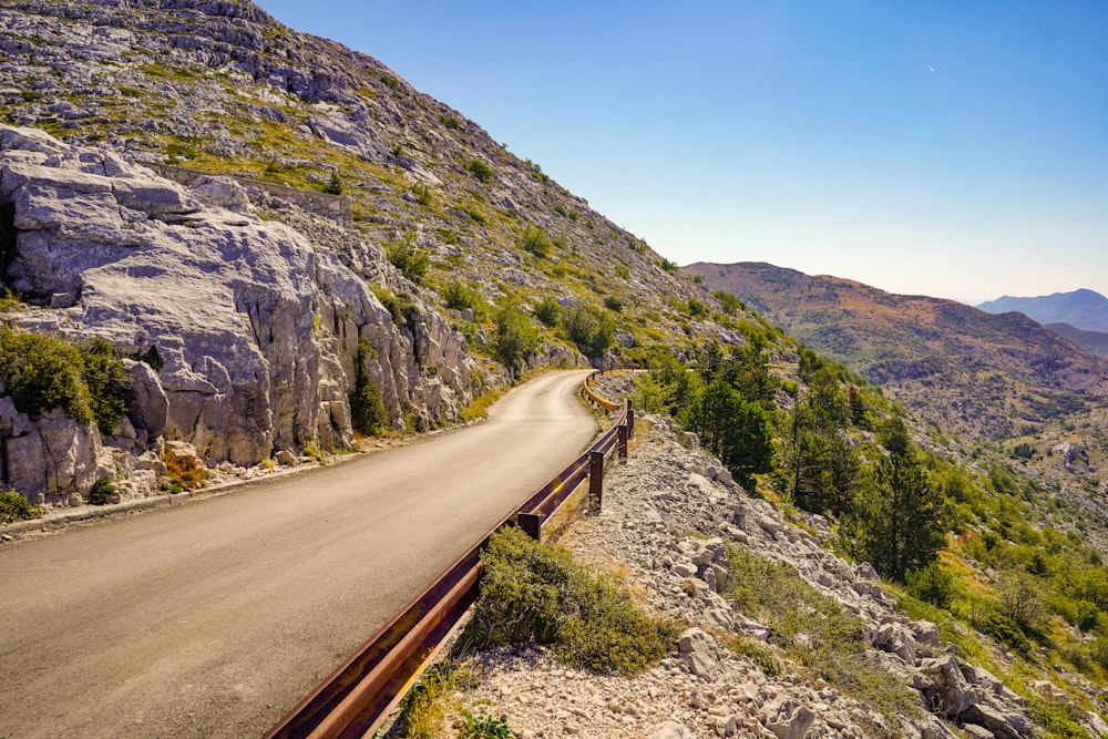 gray concrete road near green and brown mountain under blue sky during daytime