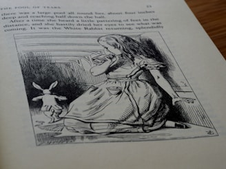 An illustration on a page from a book, depicting a young girl with long hair wearing a dress, sitting on the ground while looking towards a rabbit running away. The scene is sketched in a classic style, and the surrounding text describes the 'Pool of Tears' chapter.