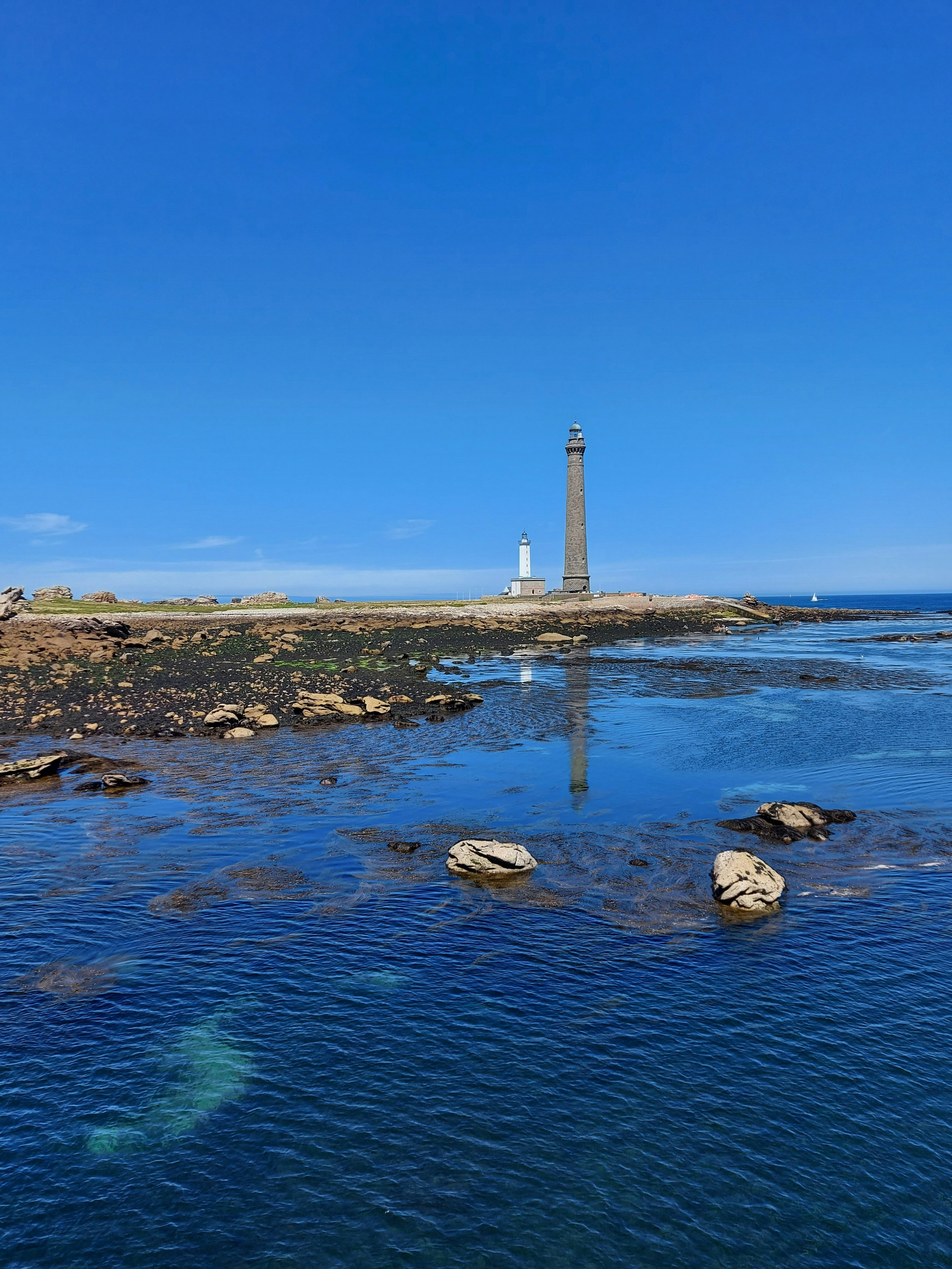 weiß-schwarzer Leuchtturm auf braunem Sand in der Nähe von Gewässern unter blauem Himmel tagsüber