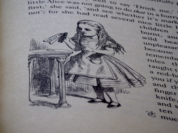 An illustration of a young girl holding a bottle labeled 'Drink Me', standing in front of a table. The image is part of a page from a book with visible text around the drawing.