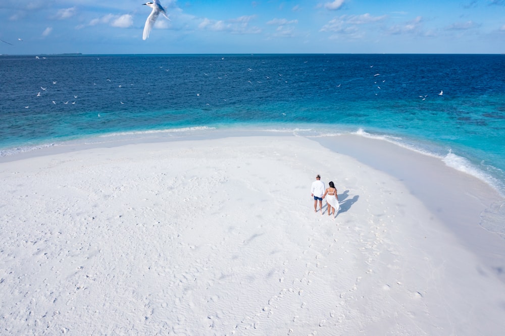 2 person in white shirt and black pants walking on white sand beach during daytime