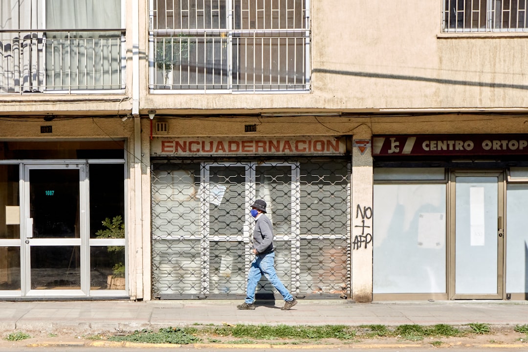 man in blue denim jeans walking on sidewalk near brown concrete building during daytime