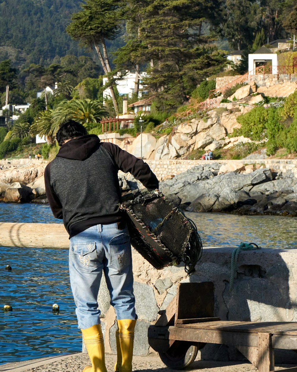 man in black hoodie and blue denim jeans standing beside body of water during daytime