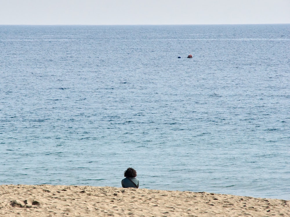 woman in black shirt sitting on brown sand near body of water during daytime
