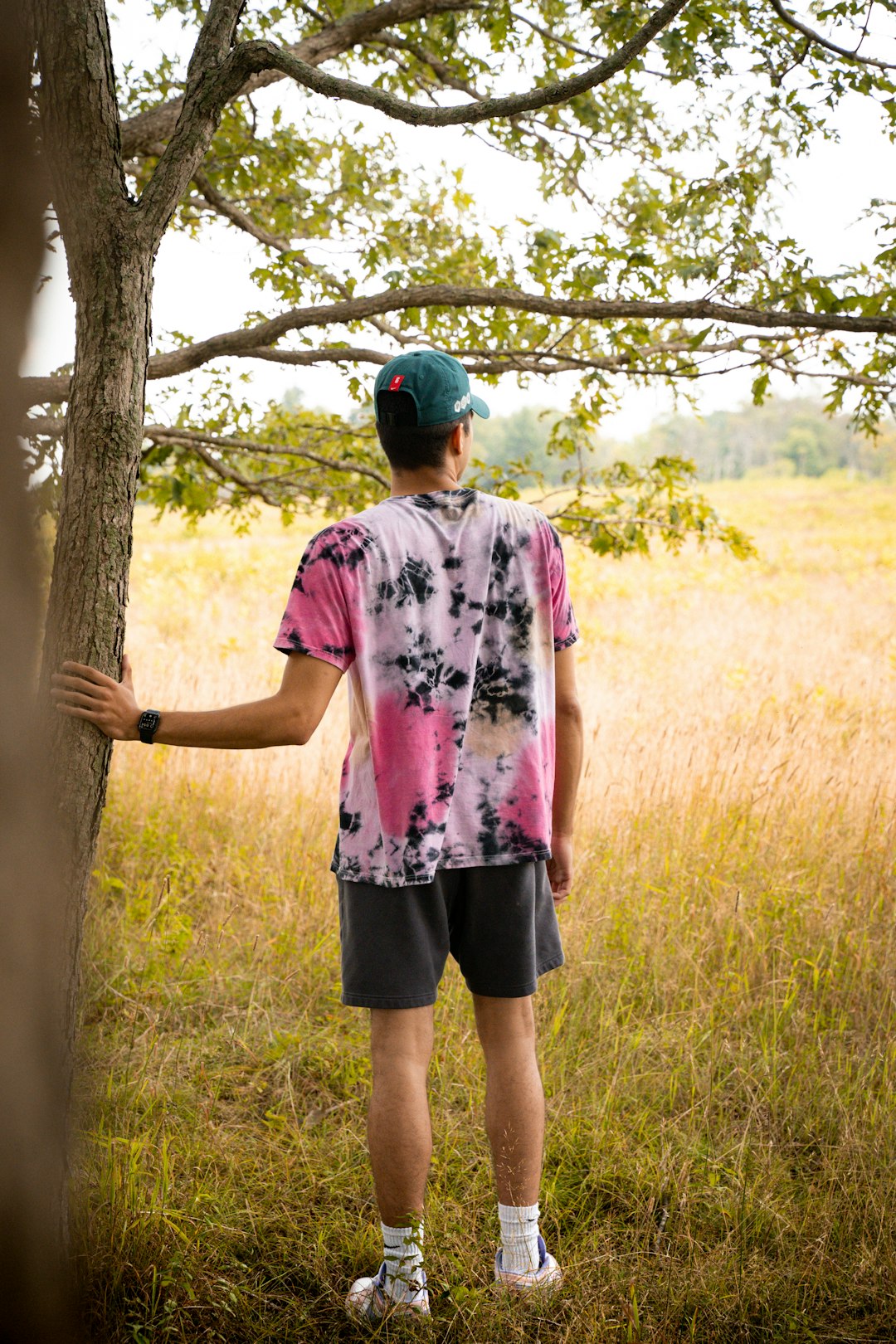 man in pink and white floral t-shirt standing beside brown tree during daytime