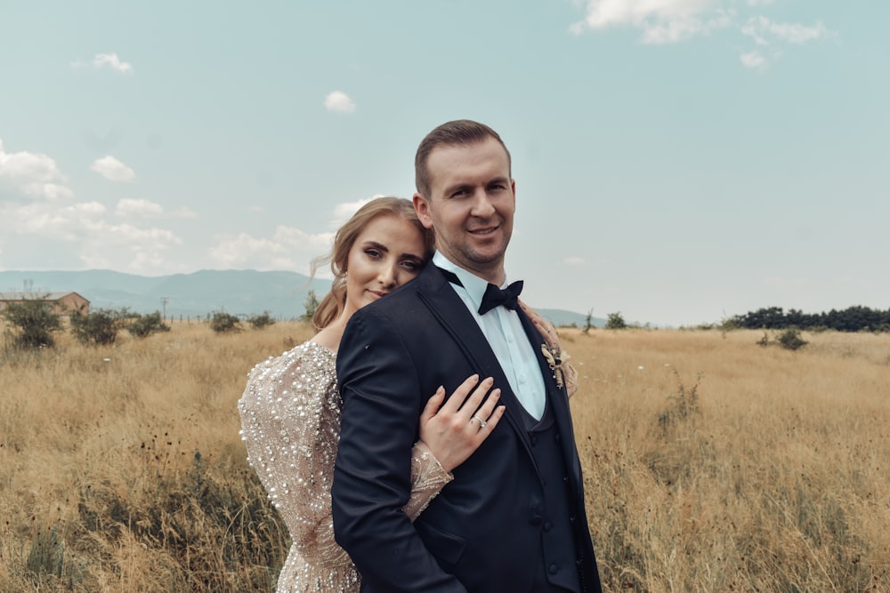 man in black suit jacket hugging woman in white floral lace dress