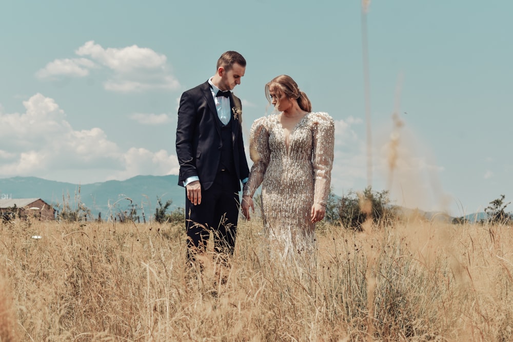 man in black suit standing beside woman in white long sleeve shirt on brown grass field