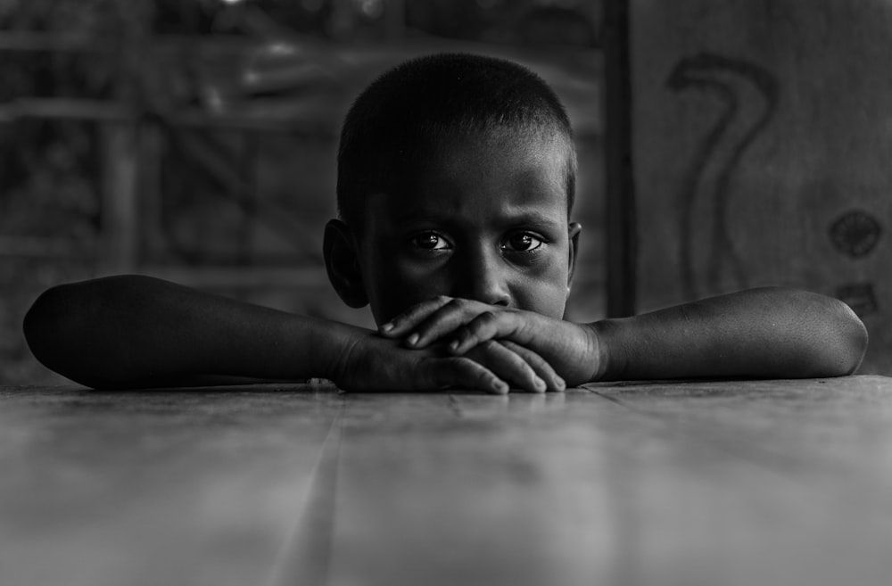 grayscale photo of boy leaning on table