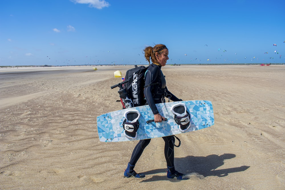 woman in black jacket sitting on blue and white skateboard on beach during daytime