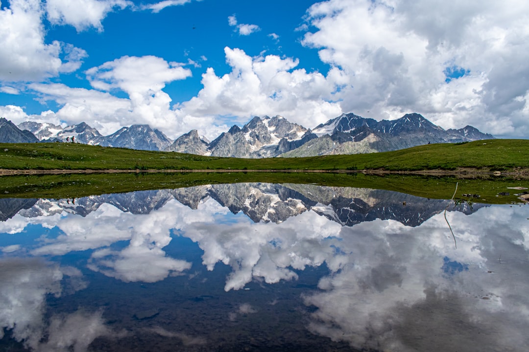 green grass field near lake under blue sky and white clouds during daytime