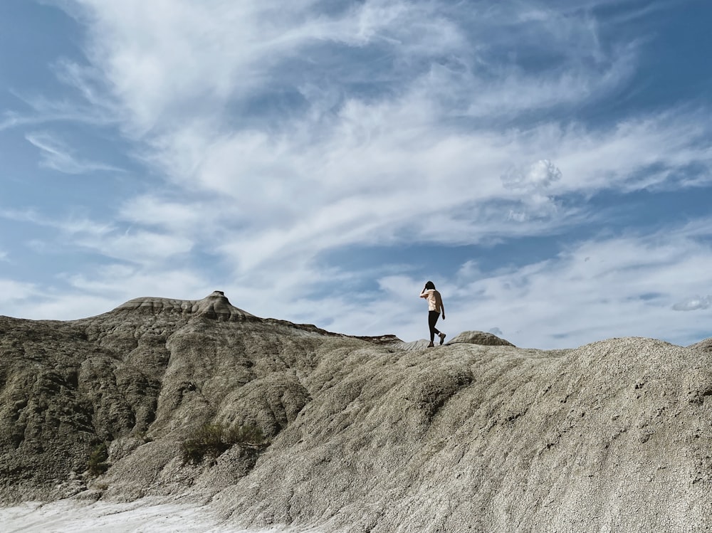 woman in black tank top and black shorts standing on brown rock formation under blue and