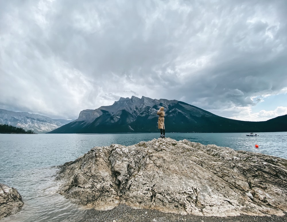 woman in black jacket standing on gray rock formation near body of water during daytime