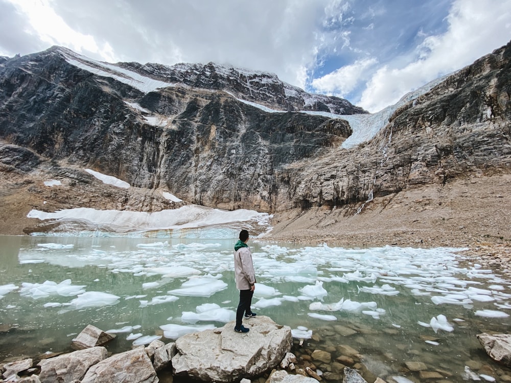 homme en veste noire debout sur un rocher près du lac pendant la journée