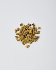A pile of small, dried, tightly-coiled flower buds with a greenish-brown color scattered on a plain white background.
