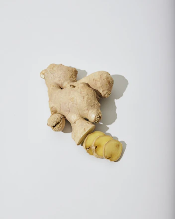 Close-up of Slim Sana capsules next to fresh ginger root on a wooden table.