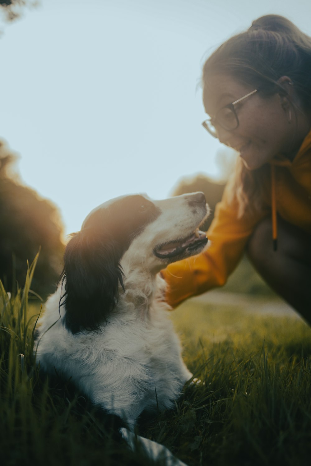 woman in brown jacket kissing white and brown long coated dog