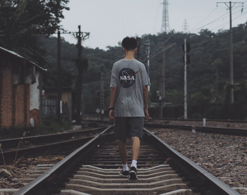 man in gray crew neck t-shirt and black shorts walking on train rail during daytime