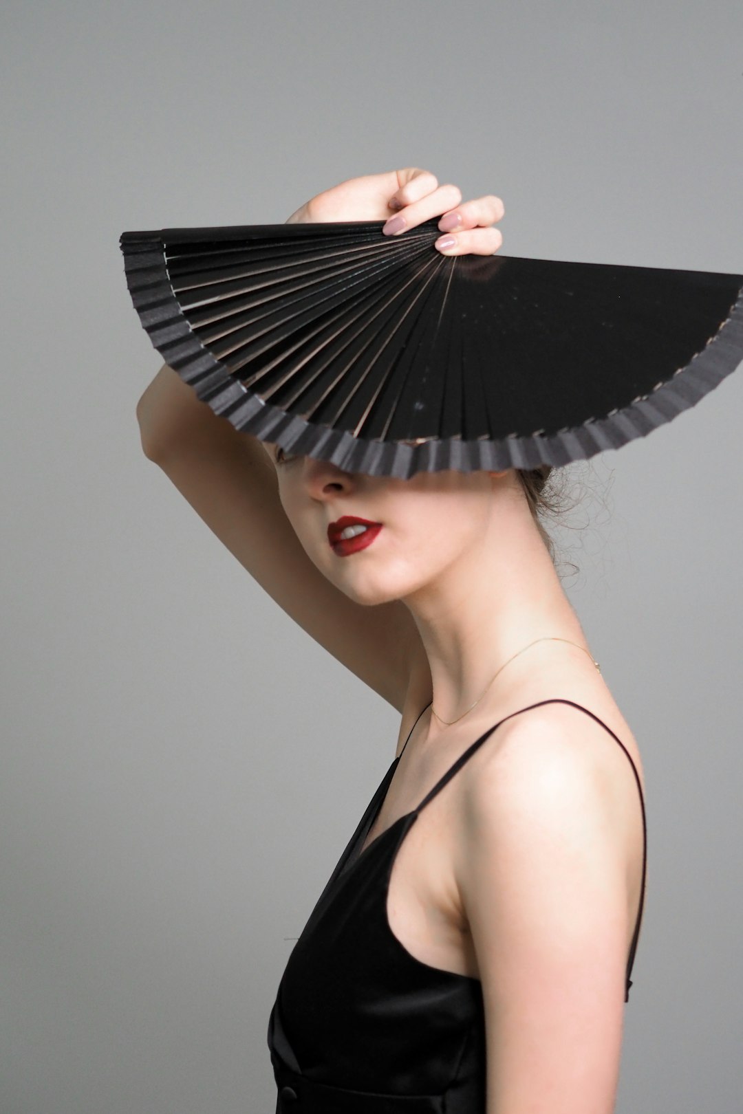 woman in black spaghetti strap top holding black hand fan