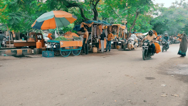 Scooters lined up outside a vibrant local market bustling with fresh tropical fruits and spices.