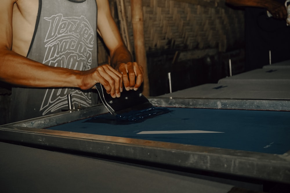 man in white tank top standing beside blue and silver table