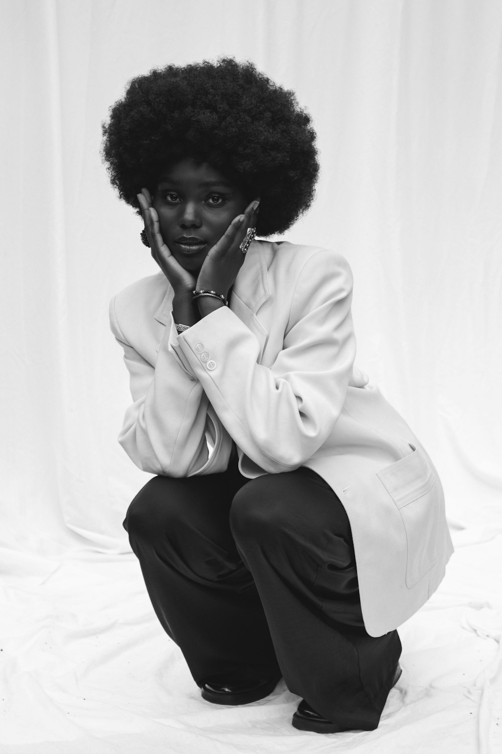 woman in white coat and black pants sitting on white textile