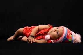 baby in red shirt lying on black textile