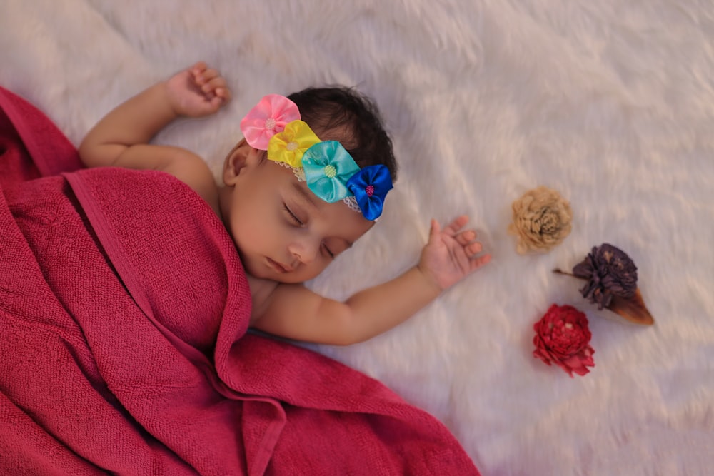 baby in pink shirt lying on white textile