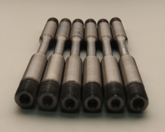 A group of identical metallic rods arranged in parallel with threaded ends placed on a neutral background. The rods have a smooth, machined finish and are aligned symmetrically.