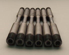 A group of identical metallic rods arranged in parallel with threaded ends placed on a neutral background. The rods have a smooth, machined finish and are aligned symmetrically.