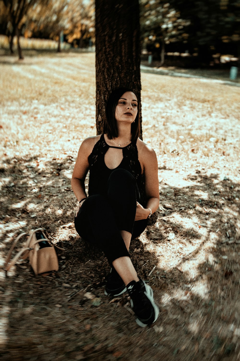 woman in black tank top and black pants sitting on brown tree trunk during daytime