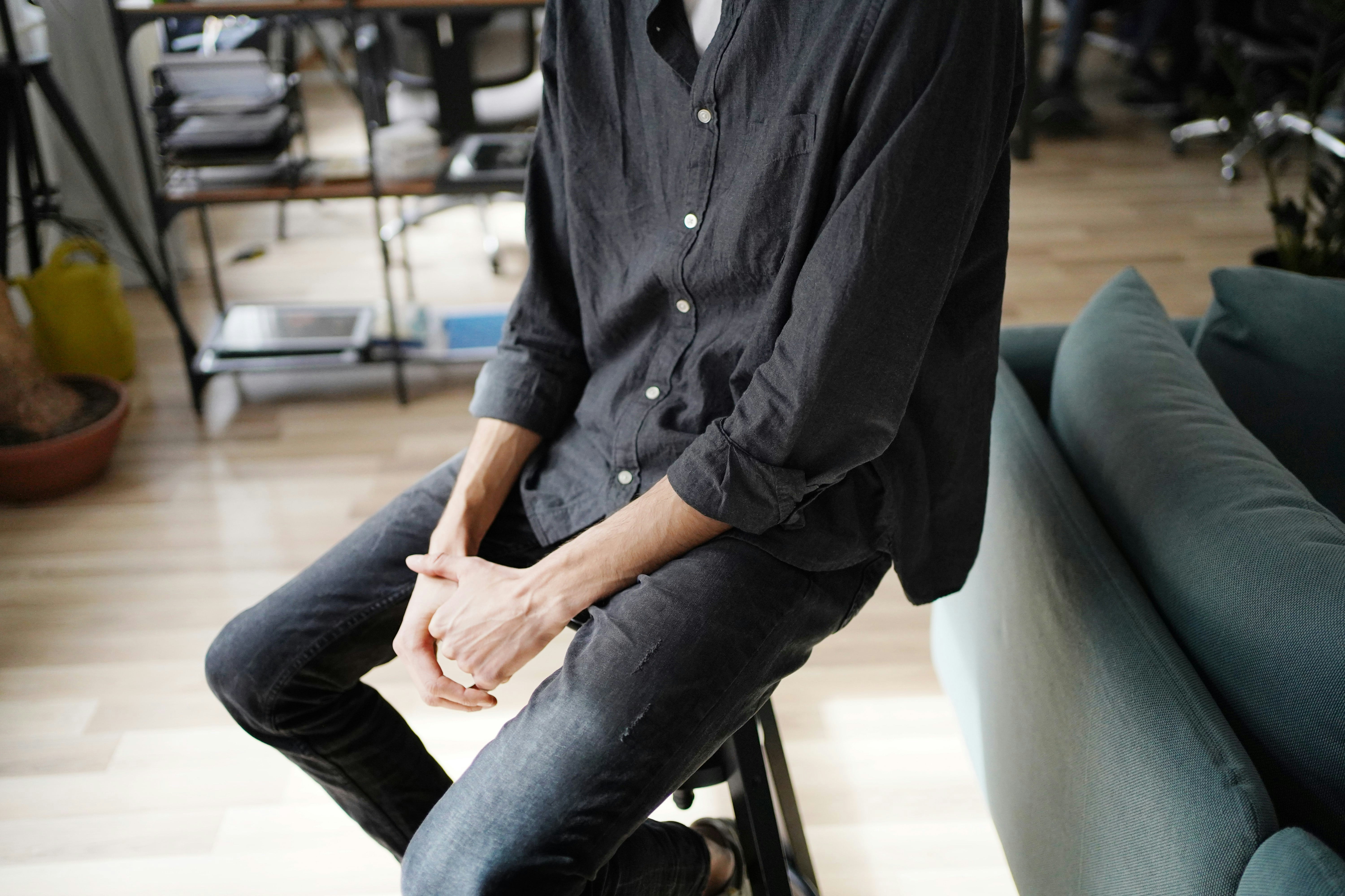 man in black dress shirt and blue denim jeans sitting on black leather chair