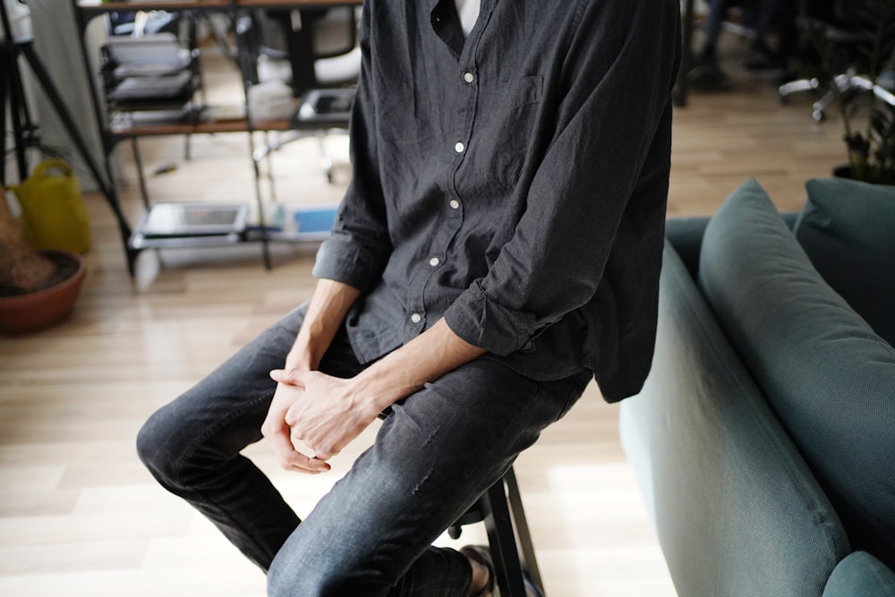 man in black dress shirt and blue denim jeans sitting on black leather chair