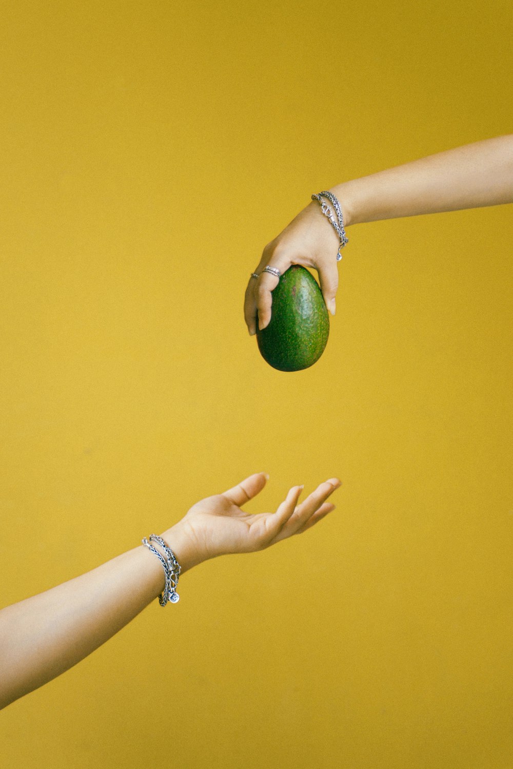 person holding green fruit on yellow background