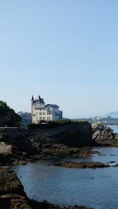 An elegant seaside mansion with white stone exterior, large terraces, and views of calm blue waters.