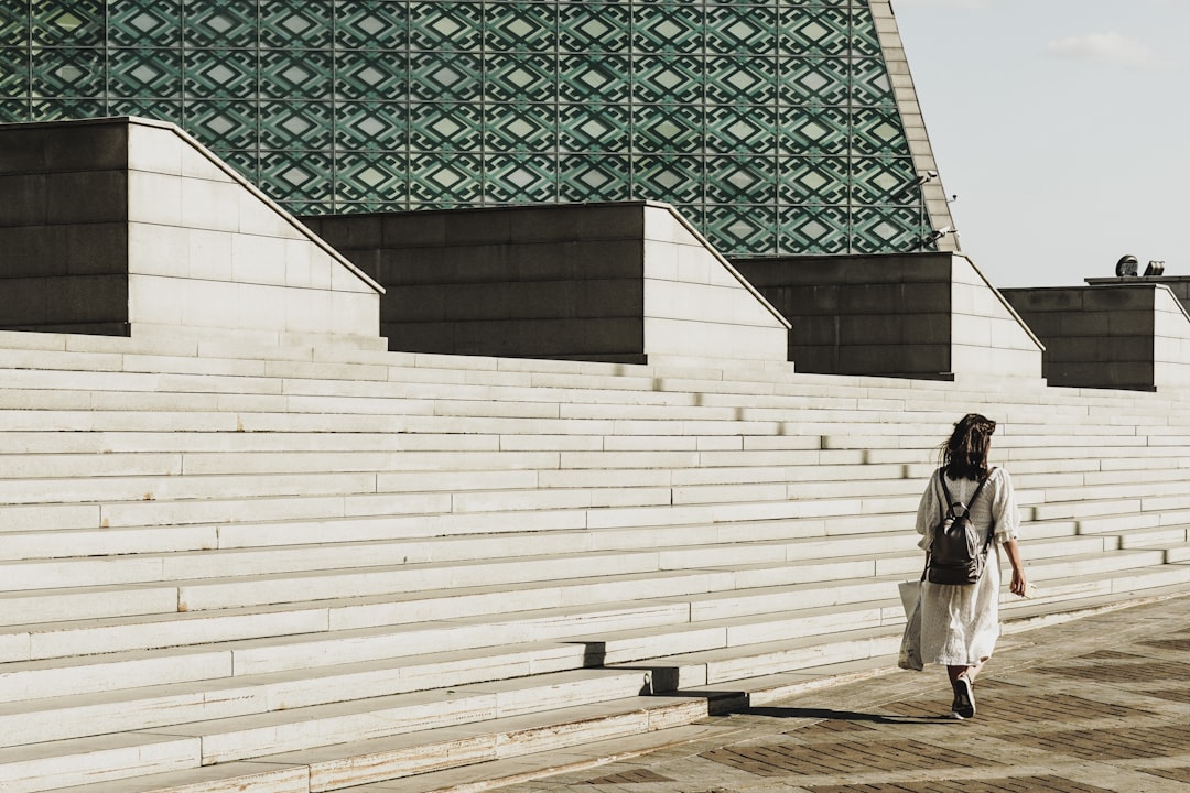 woman in white coat walking on sidewalk during daytime