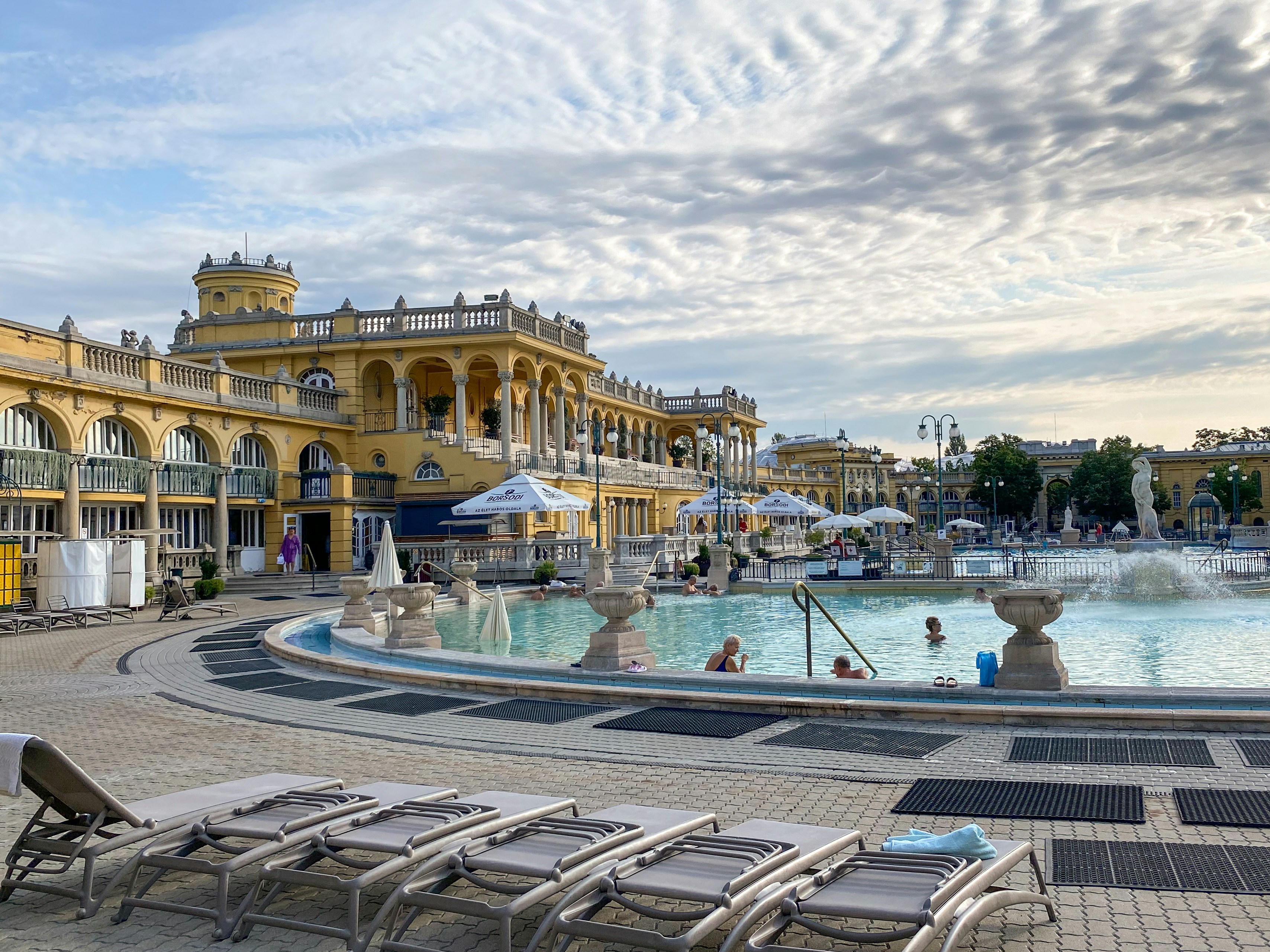 people walking on sidewalk near body of water during daytime, The Szechenyi Baths in the morning