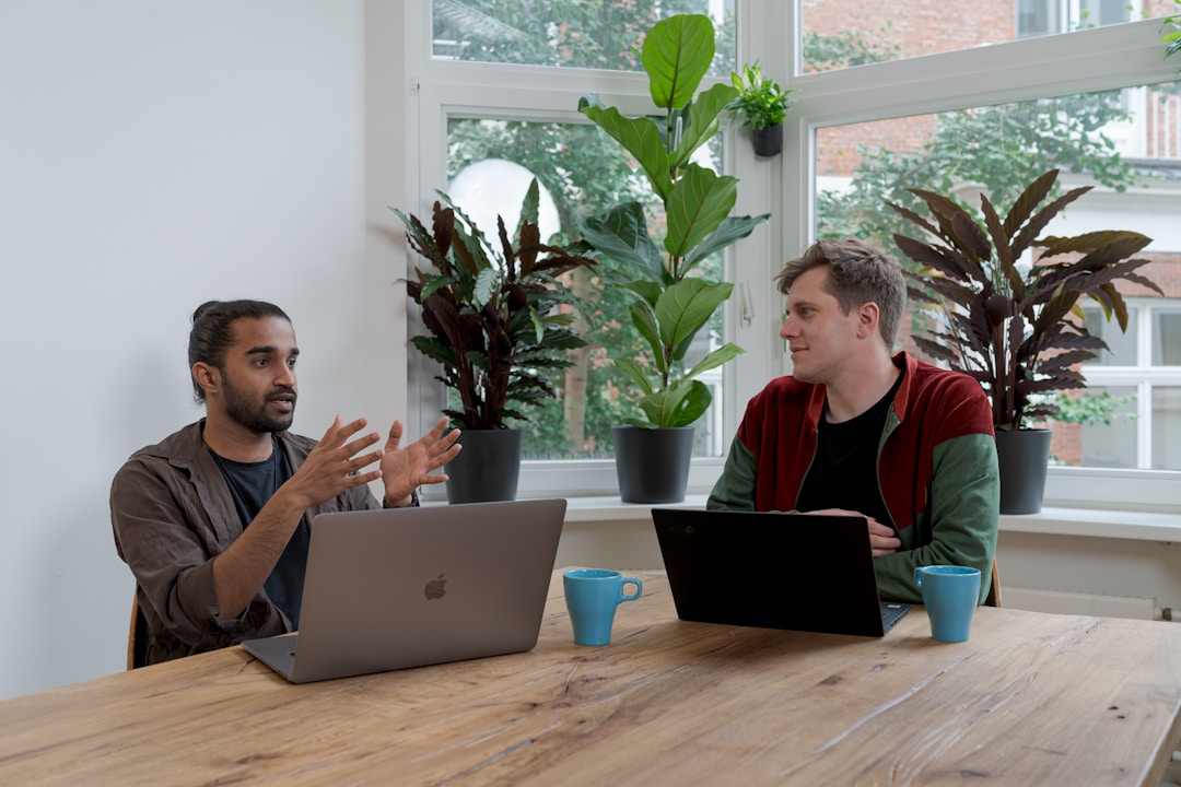 Two men seated at a table, working on laptops, discussing best practices for effective AI orchestration.