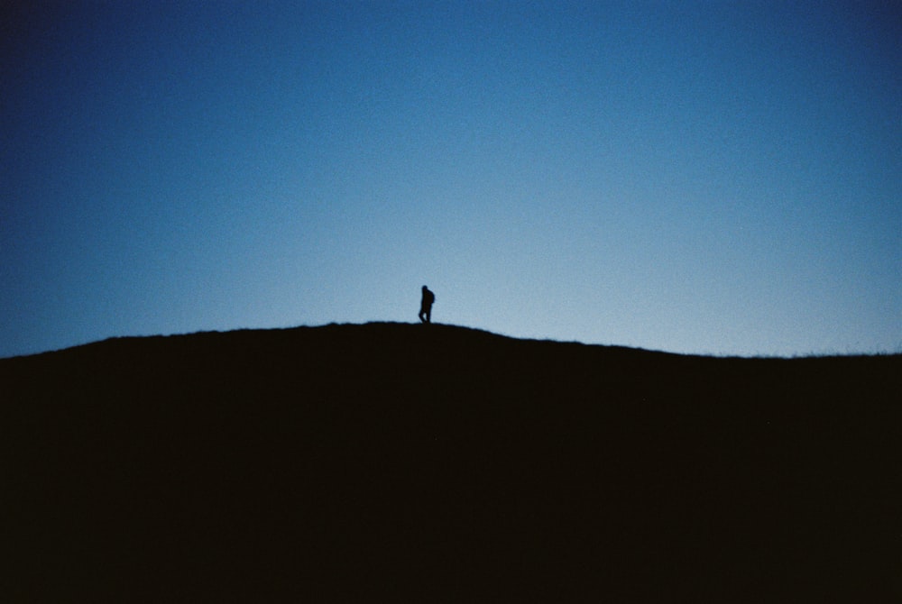 silhouette of person standing on hill during daytime