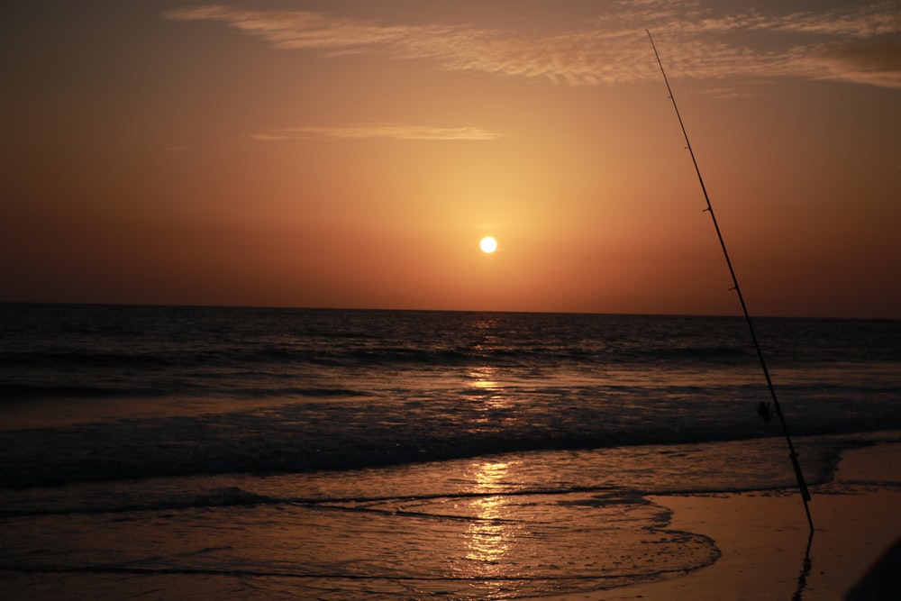 silhouette of person fishing on sea during sunset