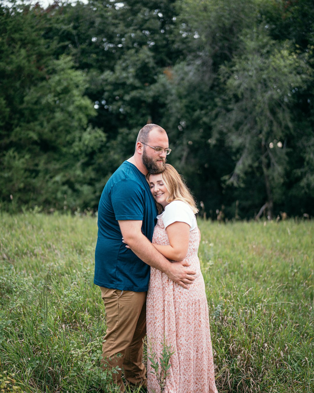 man in blue polo shirt hugging woman in brown dress on green grass field during daytime