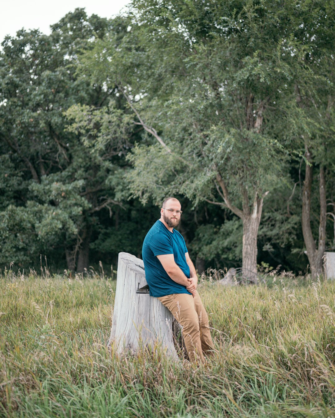 man in blue long sleeve shirt and brown pants sitting on white wooden log during daytime