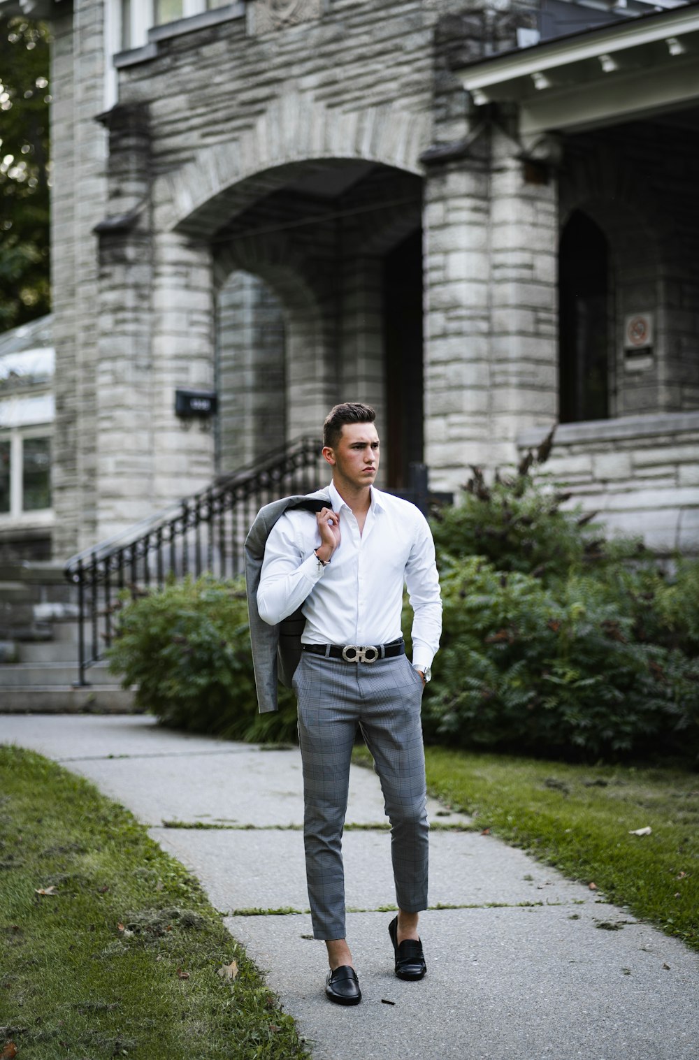 man in white dress shirt and blue denim jeans standing on gray concrete pathway during daytime