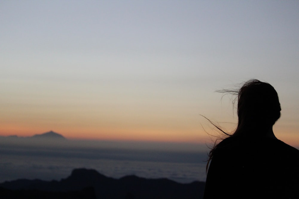 silhouette of woman standing on mountain during sunset