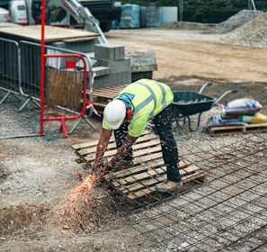 man in green and yellow safety vest and blue denim jeans standing on brown wooden pallet