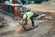 man in green and yellow safety vest and blue denim jeans standing on brown wooden pallet